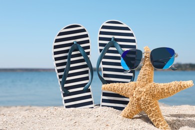 Photo of Stylish flip flops, sunglasses and starfish on sandy beach