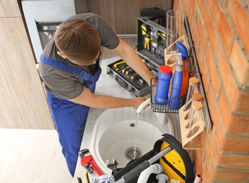 Professional plumber in uniform fixing kitchen sink