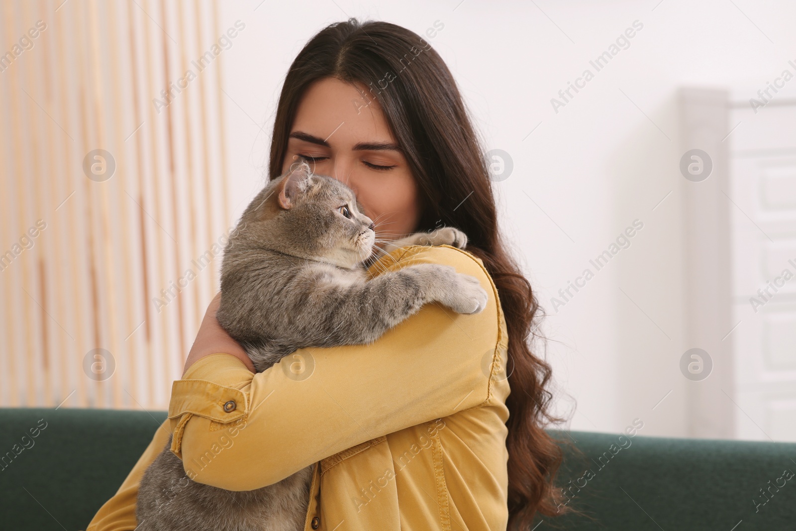 Photo of Young woman kissing her adorable cat at home, space for text