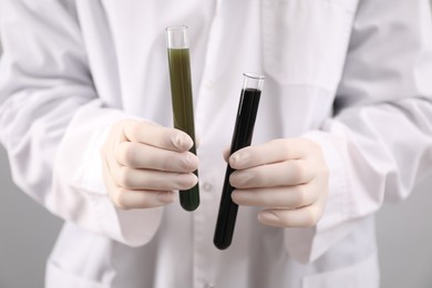 Photo of Woman holding test tubes with different types of crude oil on light background, closeup