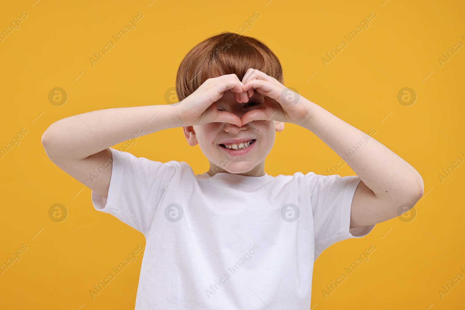 Photo of Cute little boy looking orange folded in shape of heart hands on golden background