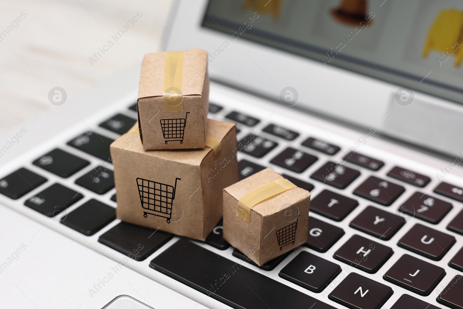 Image of Internet store. Small cardboard boxes with shopping carts and laptop on table, closeup