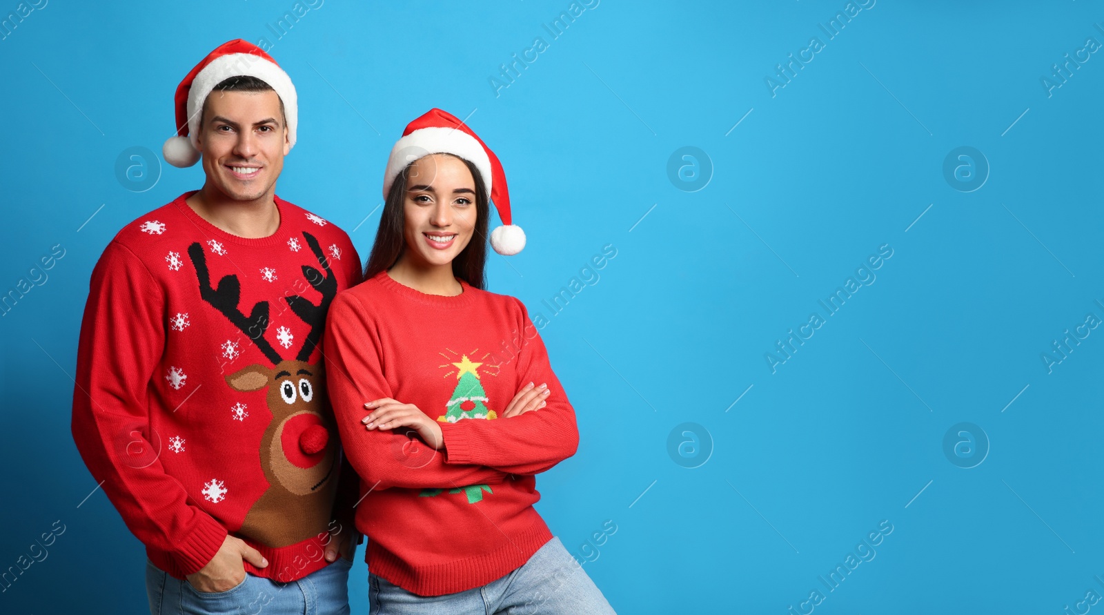 Photo of Couple in Christmas sweaters and Santa hats on blue background, space for text