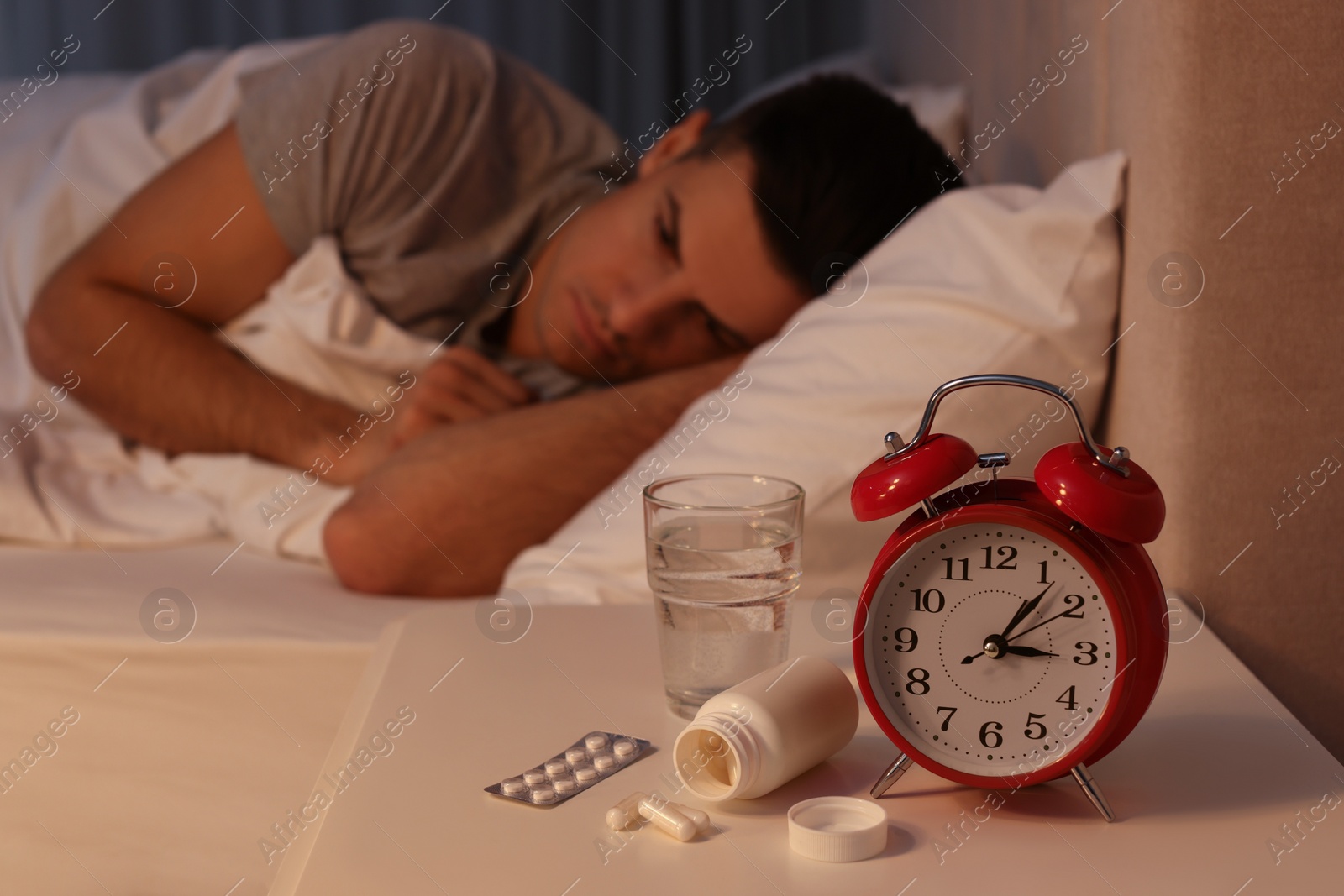 Photo of Man suffering from insomnia in bed at home, focus on pills and alarm clock