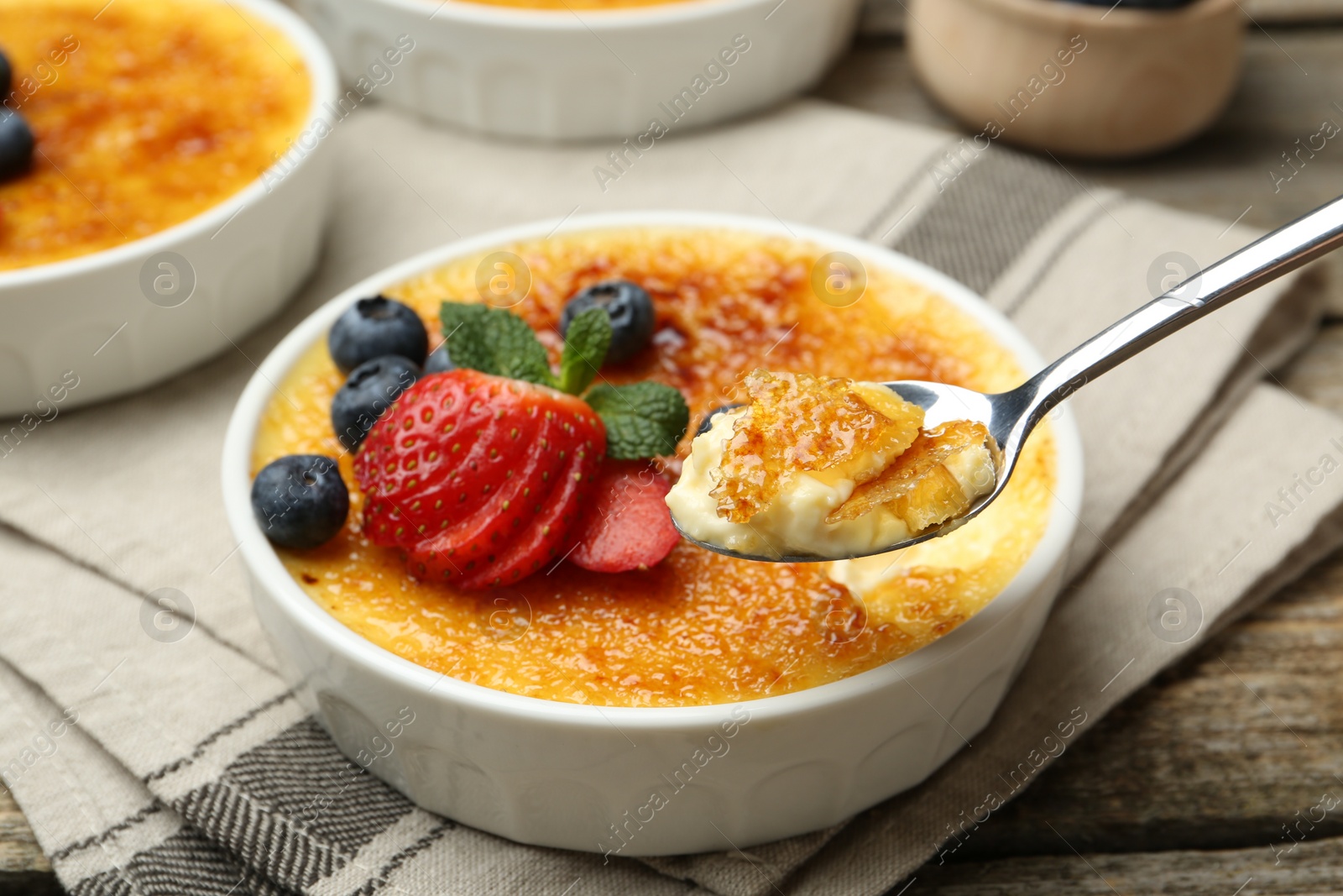 Photo of Taking delicious creme brulee with berries and mint from bowl at wooden table, closeup