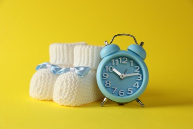 Alarm clock and baby booties on yellow background. Time to give birth