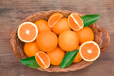 Photo of Wicker basket with ripe juicy oranges and green leaves on wooden table, top view