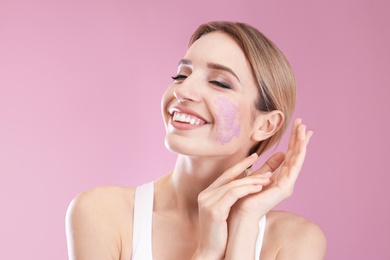 Photo of Young woman applying natural scrub on her face against color background
