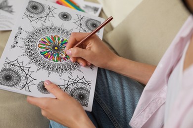 Young woman coloring antistress page on sofa, closeup