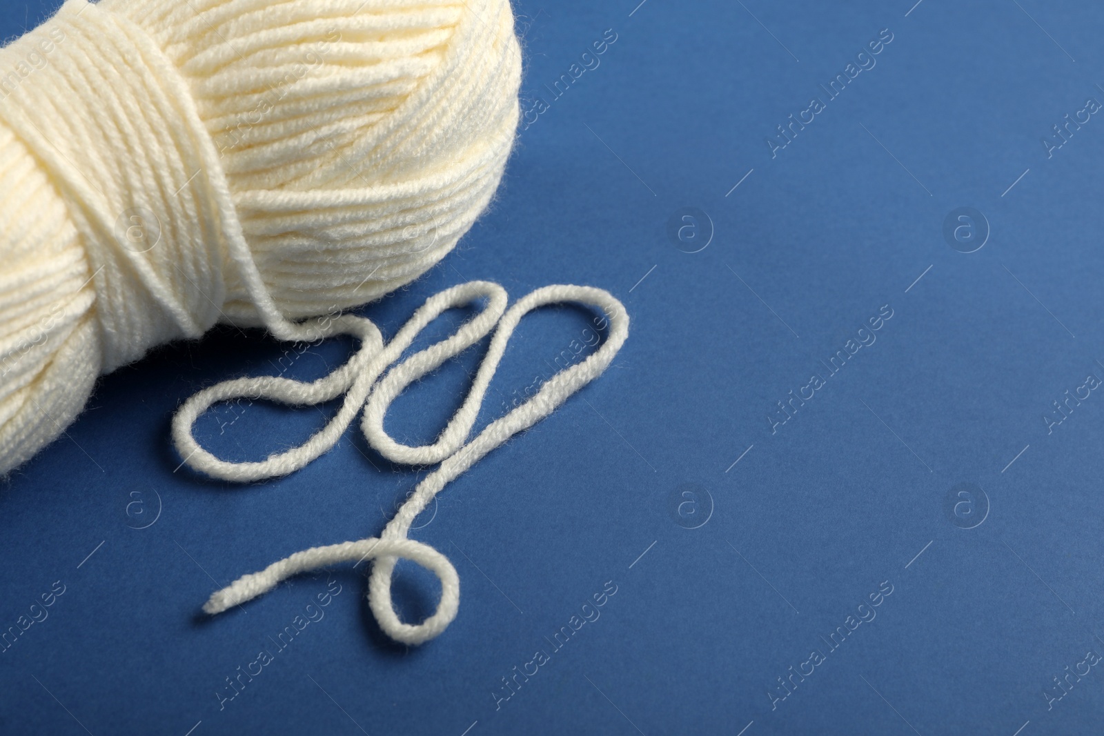 Photo of Soft white woolen yarn on blue background, closeup