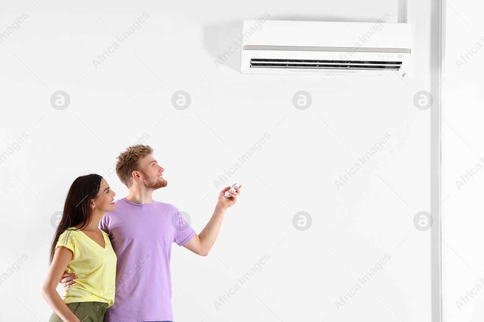 Photo of Young couple turning on air conditioner against white background