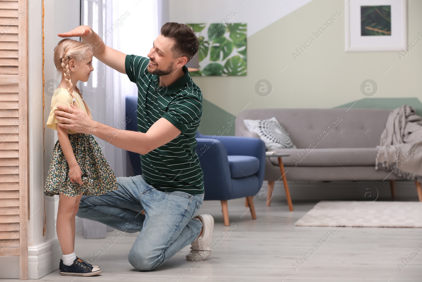 Photo of Young man measuring his daughter's height at home