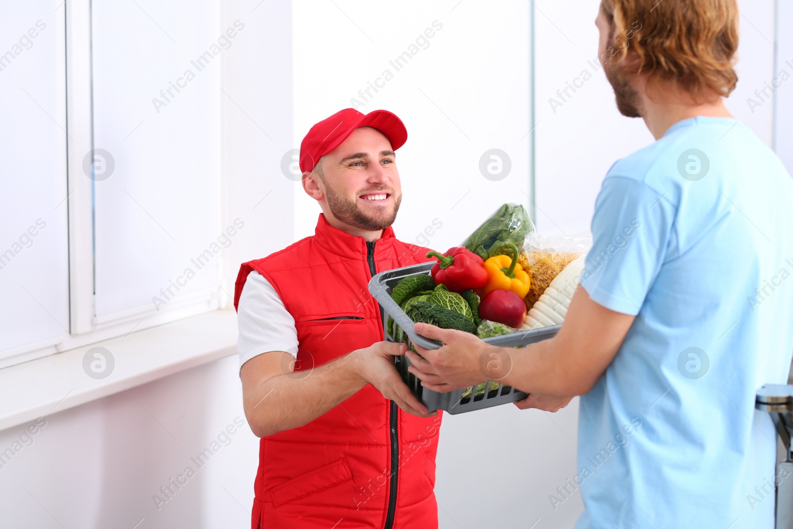 Photo of Courier giving plastic crate with products to customer at home. Food delivery service