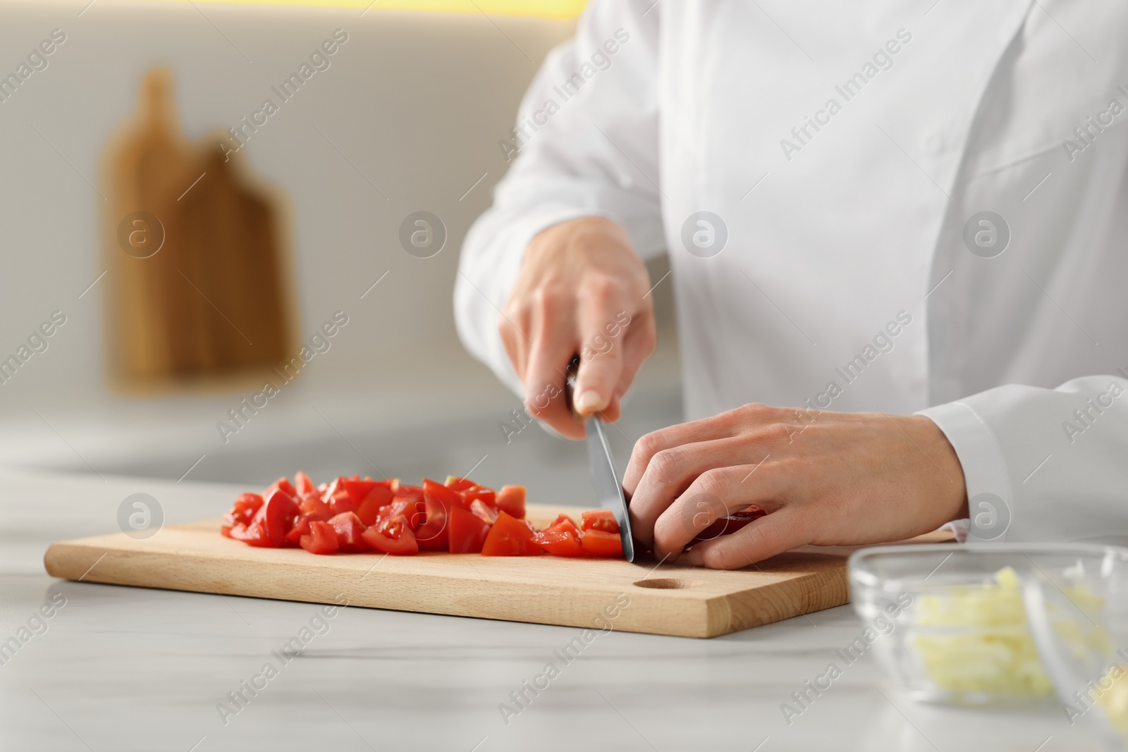 Photo of Professional chef cutting tomatoes at white marble table indoors, closeup