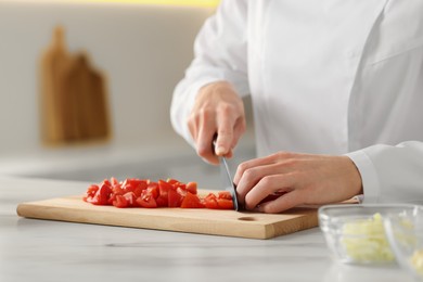 Professional chef cutting tomatoes at white marble table indoors, closeup