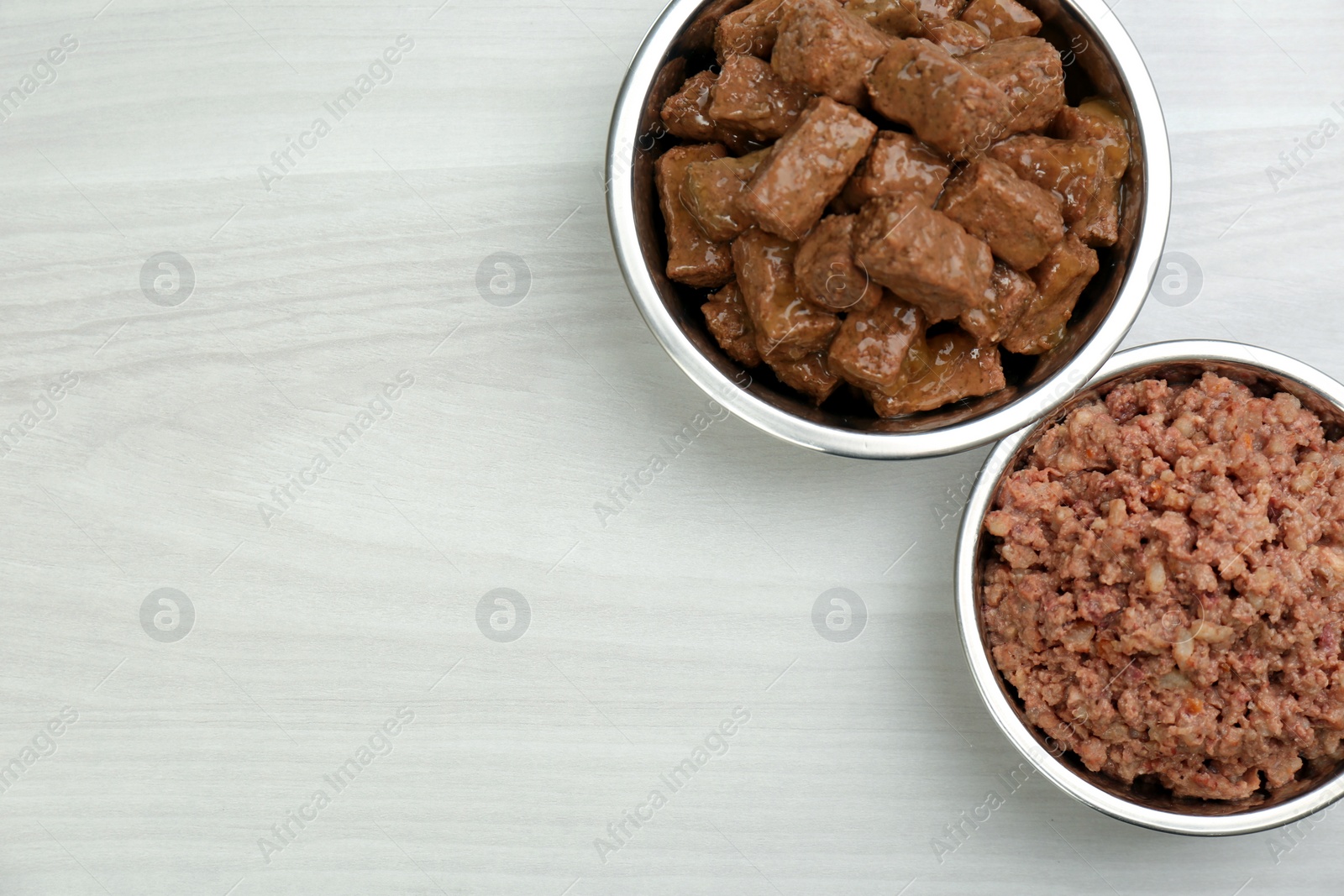 Photo of Different pet food in feeding bowls on white wooden background, flat lay. Space for text