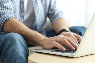 Man working on modern laptop at wooden table indoors, closeup