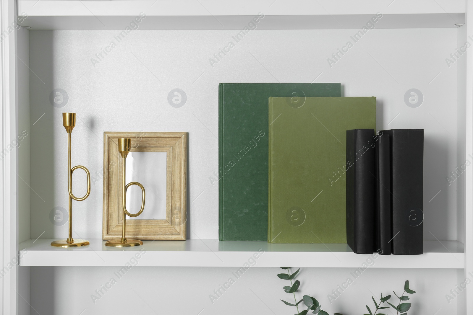 Photo of White shelf with books, candlesticks and photo frame indoors. Interior design