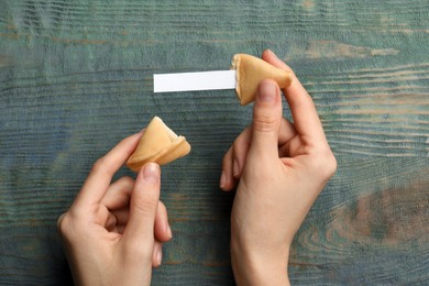 Photo of Woman holding tasty fortune cookie and paper with prediction at blue wooden table, top view. Space for text