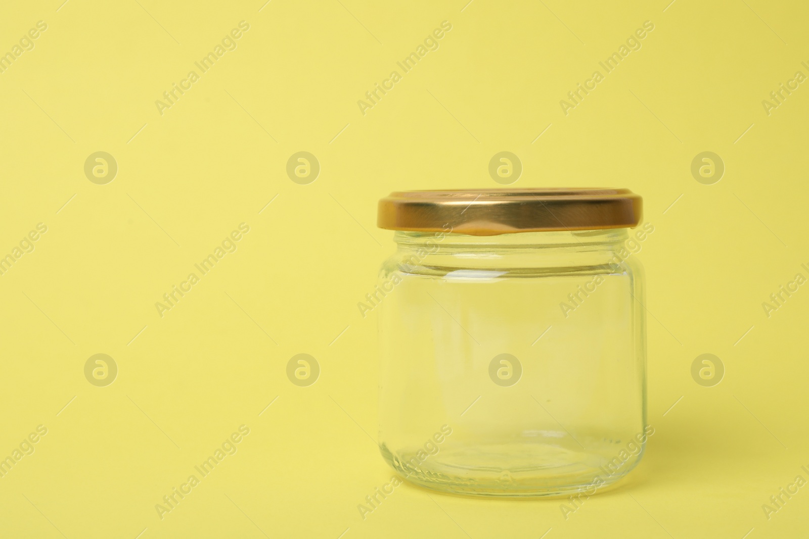 Photo of Closed empty glass jar on light yellow background, space for text