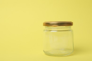 Photo of Closed empty glass jar on light yellow background, space for text