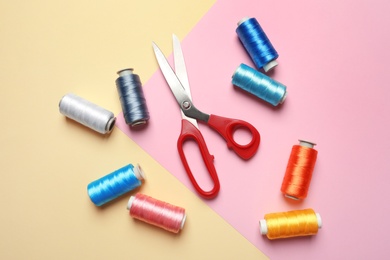 Photo of Bobbins of threads and sewing scissors on color background, flat lay