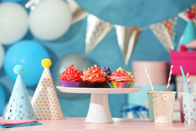 Photo of Different colorful cupcakes and party accessories on pink table