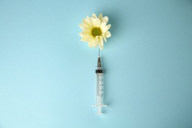 Photo of Medical syringe and beautiful chrysanthemum flower on light blue background, top view