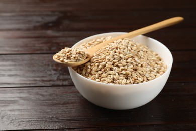 Dry pearl barley in bowl and spoon on wooden table, closeup