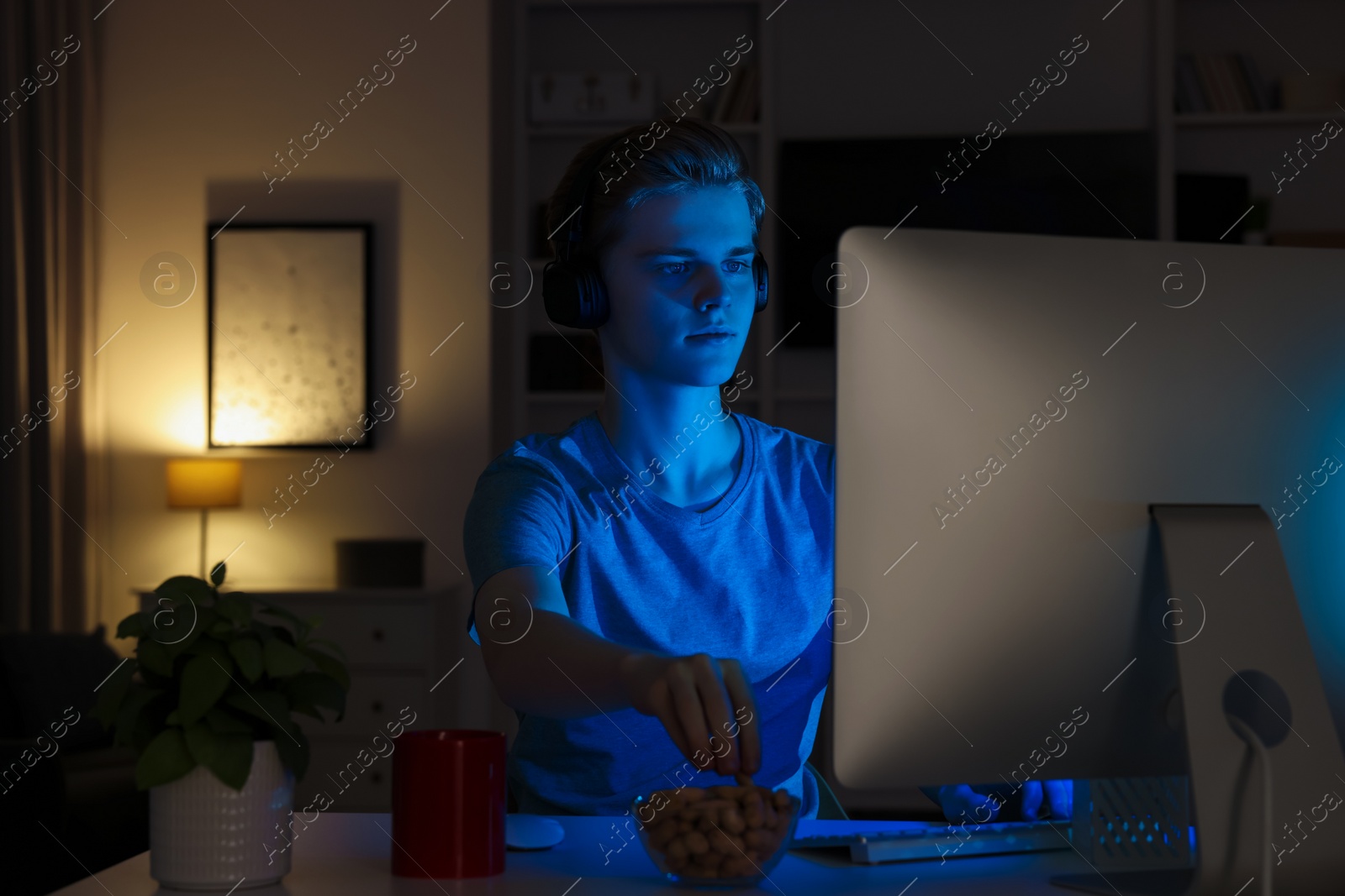 Photo of Teenage boy eating and using computer in room at night. Internet addiction