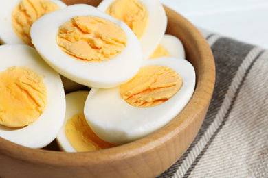 Cut hard boiled chicken eggs in wooden bowl on table, closeup