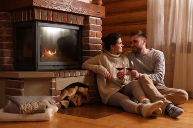 Photo of Lovely couple with glasses of wine near fireplace at home. Winter vacation