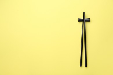 Photo of Pair of black chopsticks with rest on yellow background, top view. Space for text