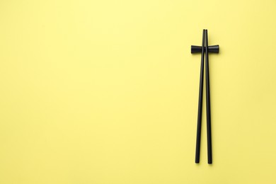 Pair of black chopsticks with rest on yellow background, top view. Space for text