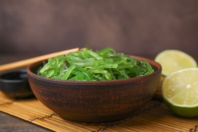 Photo of Tasty seaweed salad in bowl served on table against brown background, closeup