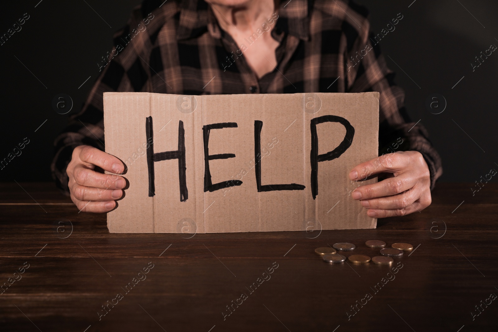 Photo of Poor mature woman holding cardboard sign HELP at table, closeup