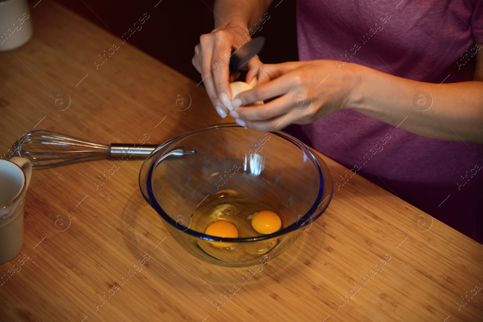 Photo of Woman breaking eggs for crepe batter in glass bowl on wooden table, closeup