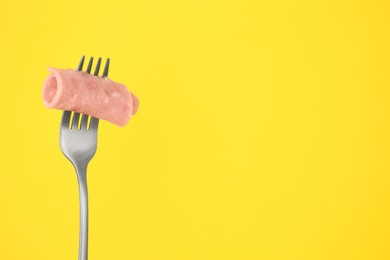 Fork with tasty slice of ham on yellow background, space for text