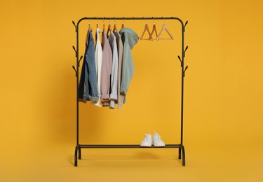 Photo of Rack with stylish clothes on wooden hangers against orange background
