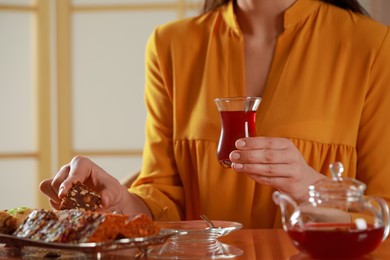 Photo of Woman with glass of traditional Turkish tea taking sweets at table indoors, closeup