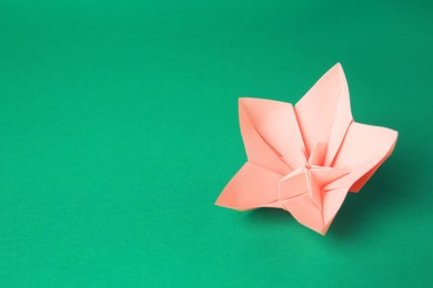 Origami art. Handmade pink paper flower on green background, space for text