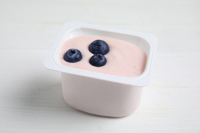 Plastic cup with tasty yogurt and blueberries on white wooden table