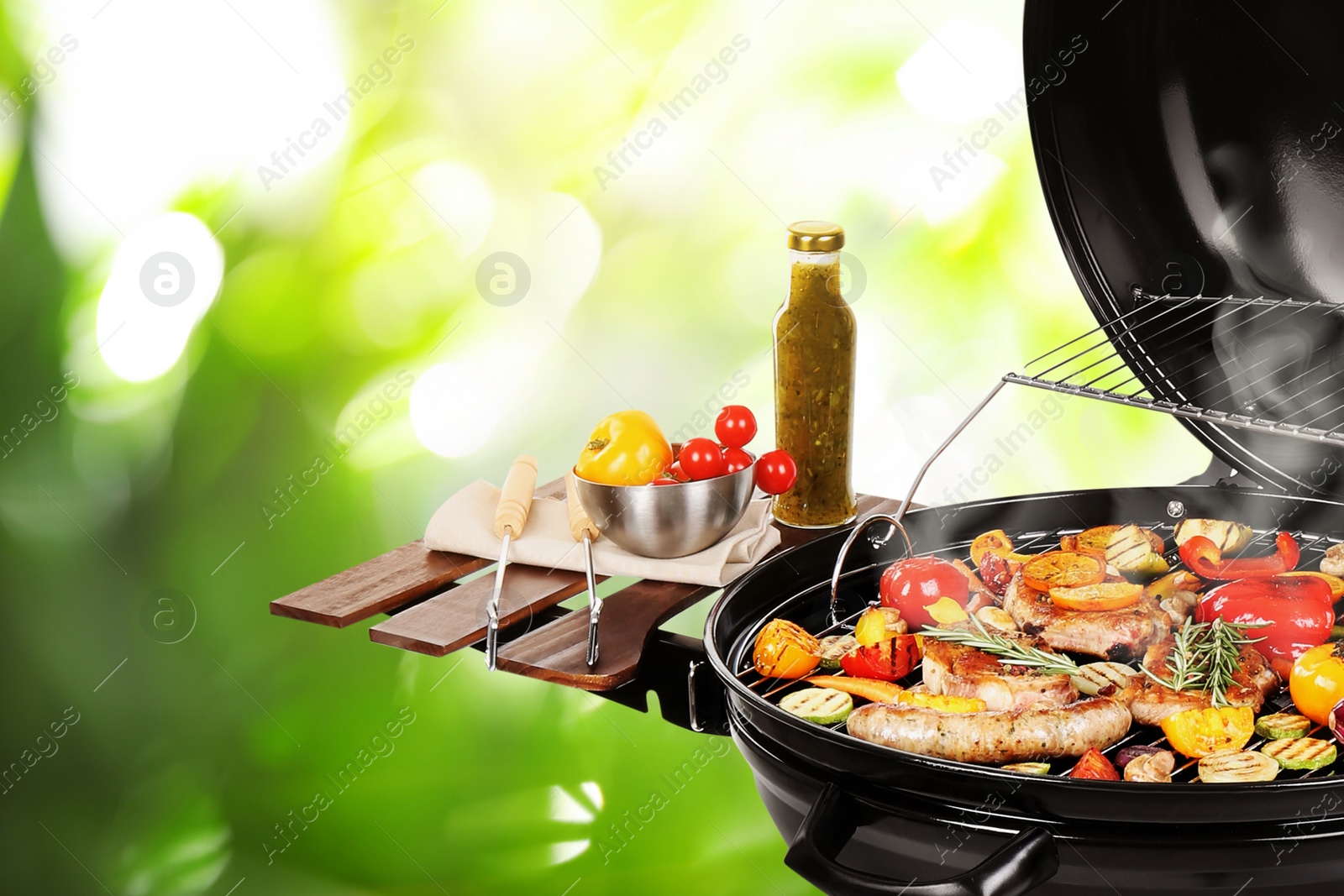 Image of Barbecue grill with meat products and vegetables on blurred green background, closeup