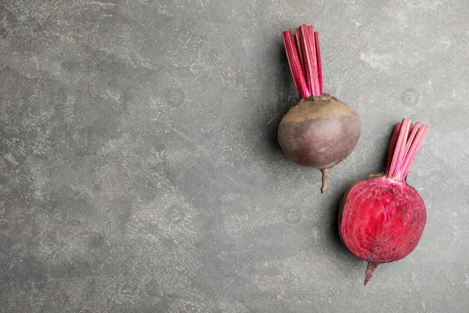 Photo of Cut and whole raw beets on grey table, flat lay. Space for text