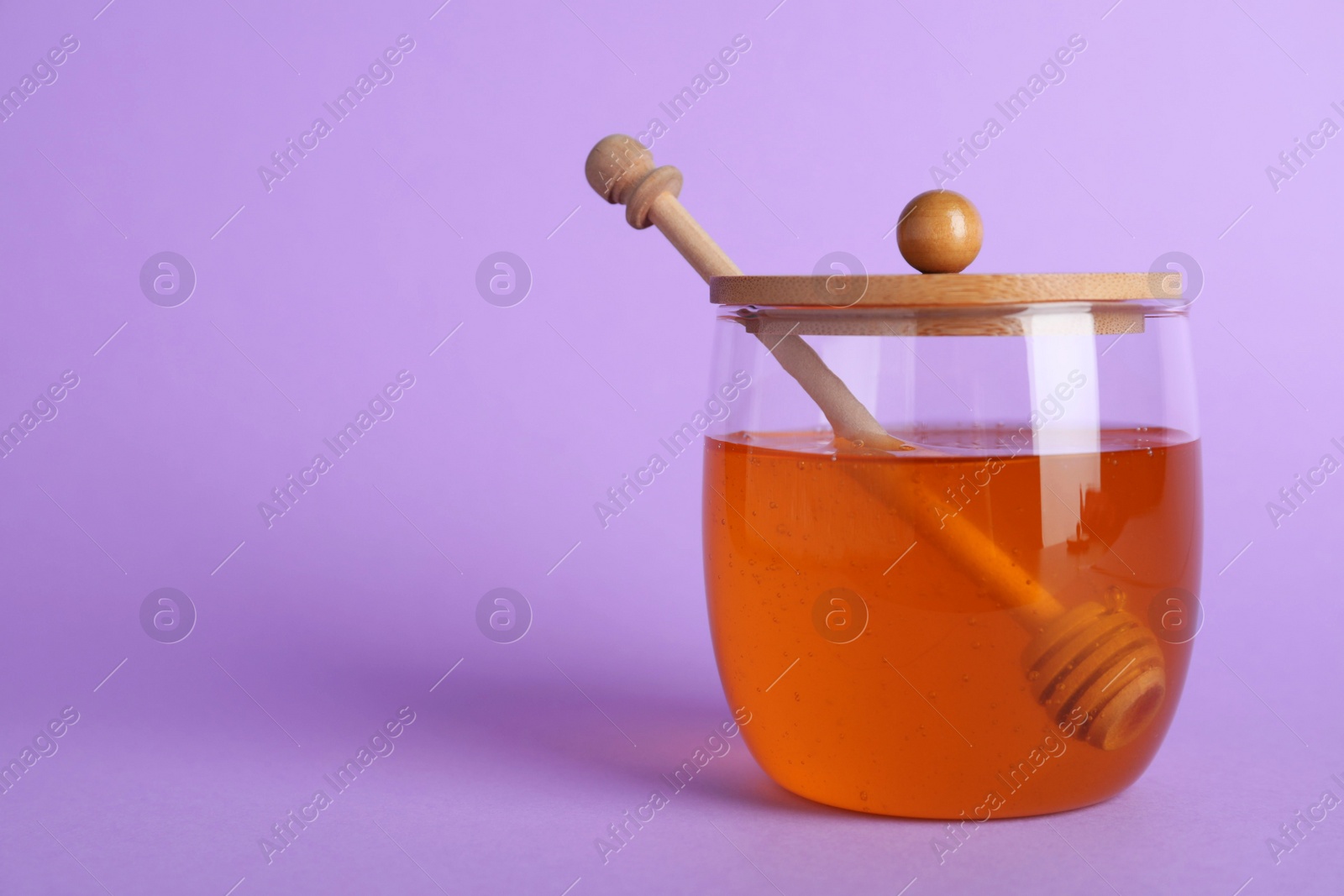 Photo of Jar of organic honey and dipper on violet background. Space for text