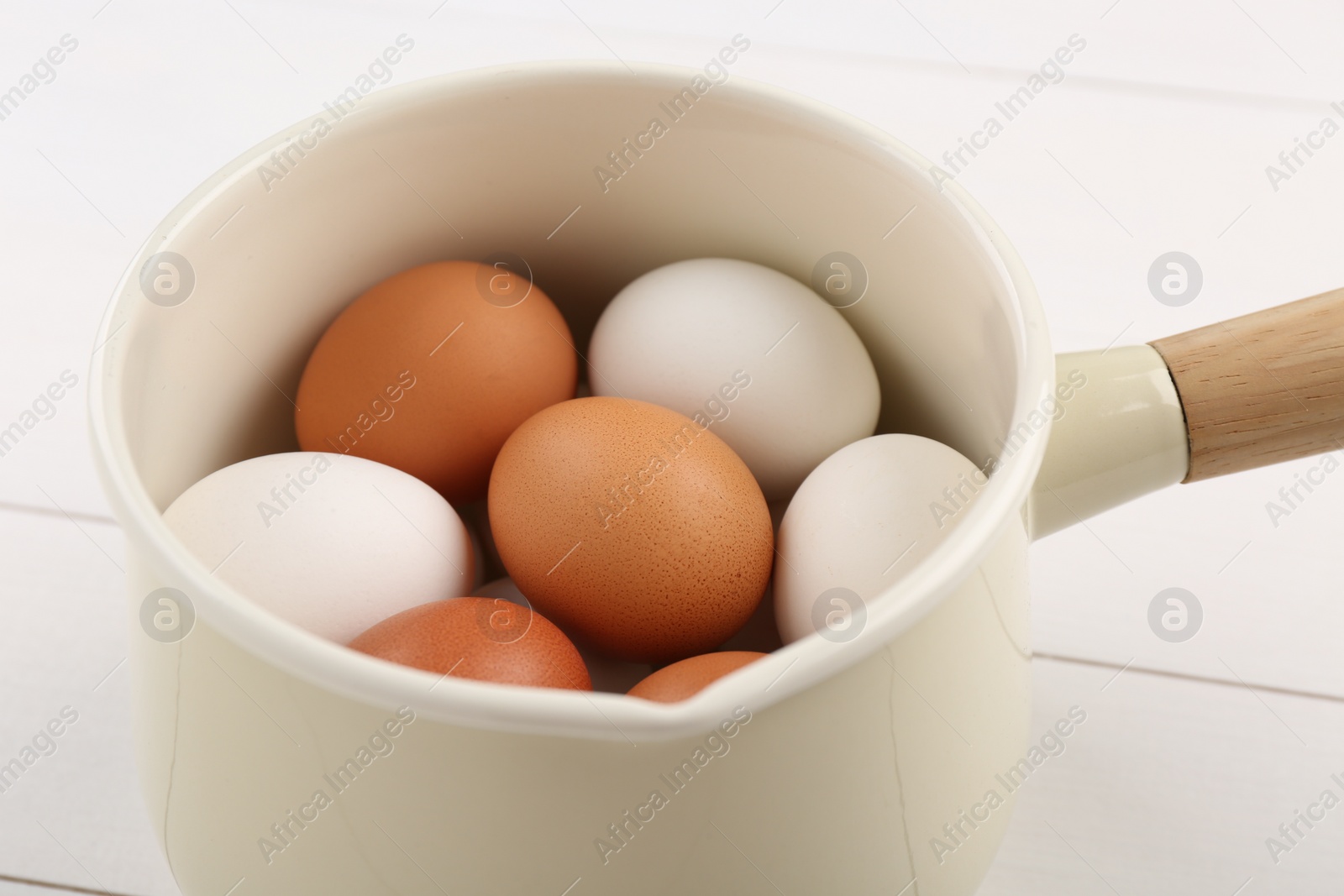 Photo of Unpeeled boiled eggs in pan on white table, closeup