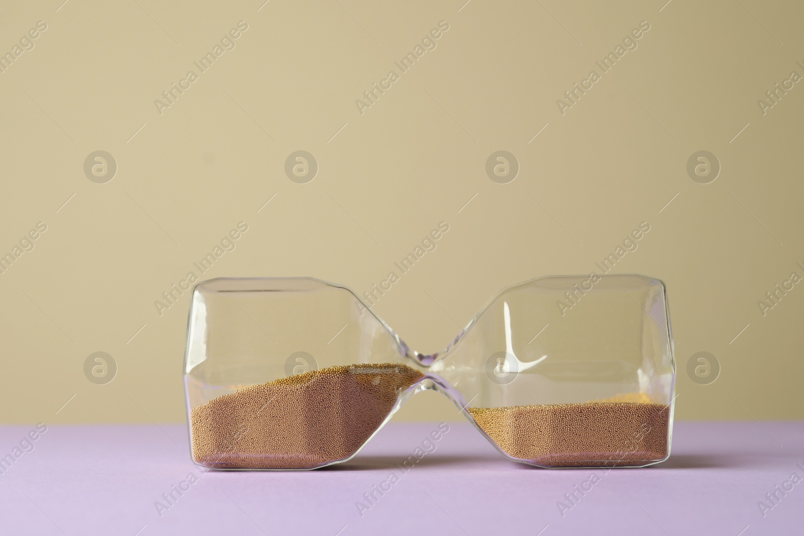 Photo of Hourglass with sand on violet table against beige background, space for text. Menopause concept