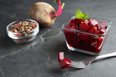 Photo of Pickled beets and fork near glass bowl on dark marble table