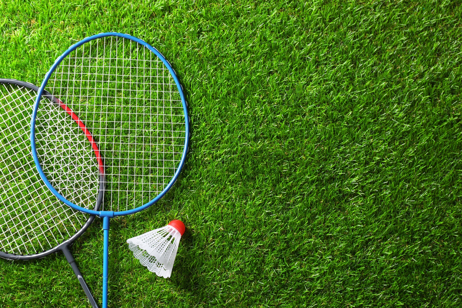 Photo of Two badminton rackets and shuttlecock on green grass, top view with space for text