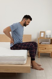 Photo of Man suffering from back pain after sleeping on uncomfortable mattress at home